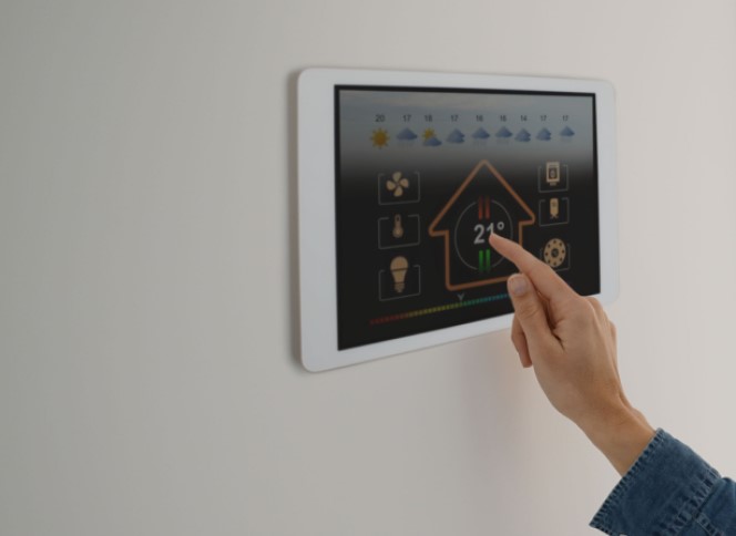 Image of a person hand changing room temperature though wall mounted device screen.